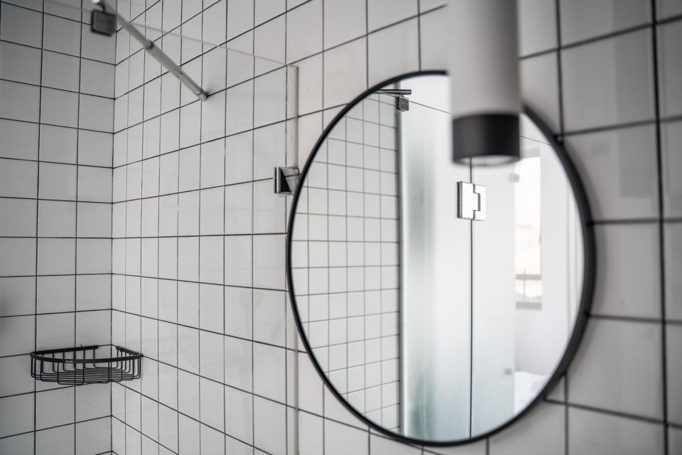 Salle de bain en carrelage blanc avec miroir rond à cadre noir