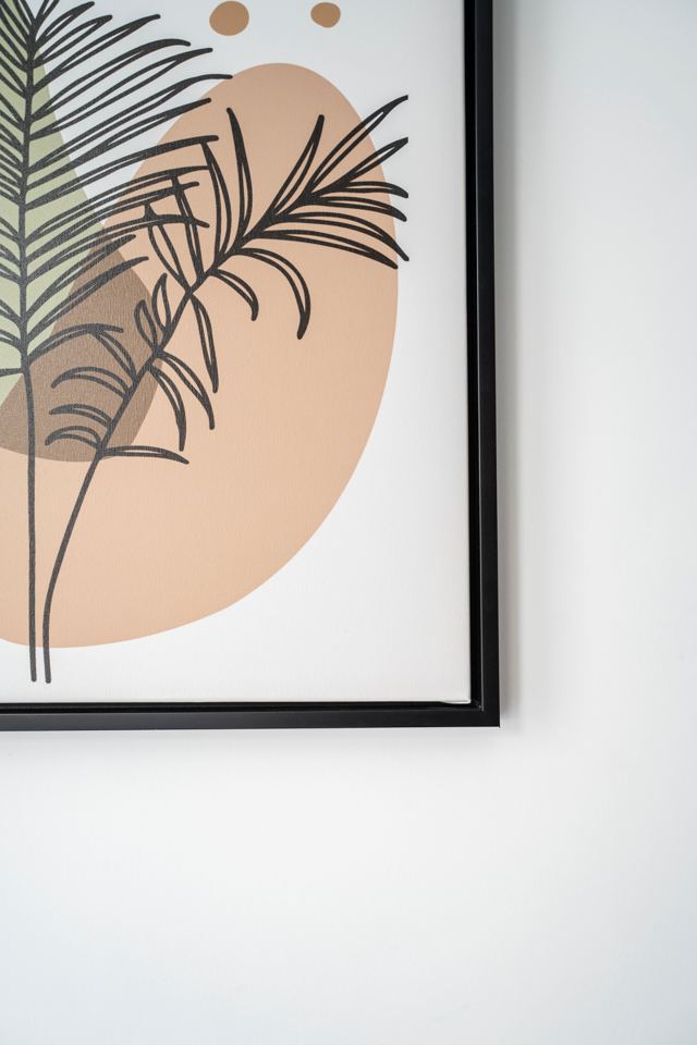 Œuvre botanique encadrée sur un mur blanc